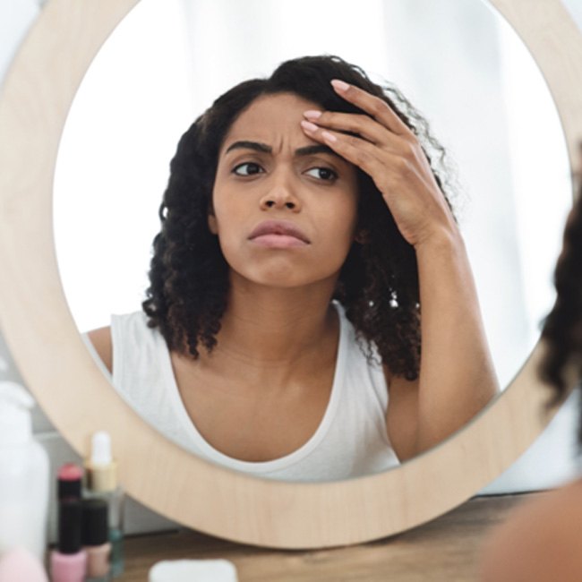 Woman frowning in mirror, concerned about fine lines