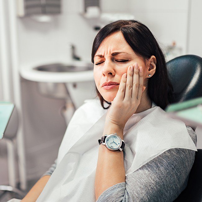 Woman holding cheek in pain during dental emergency treatment