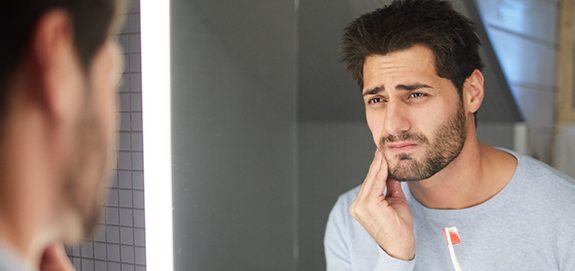 Man in need of wisdom tooth extraction holding jaw