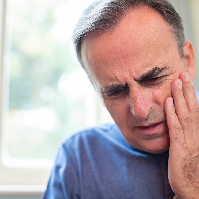 Man with dry socket holding his cheek in pain