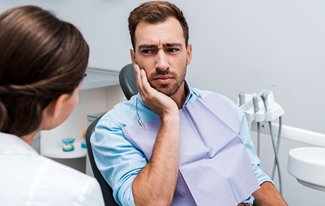 Man holding his cheek in pain while talking to an emergency dentist