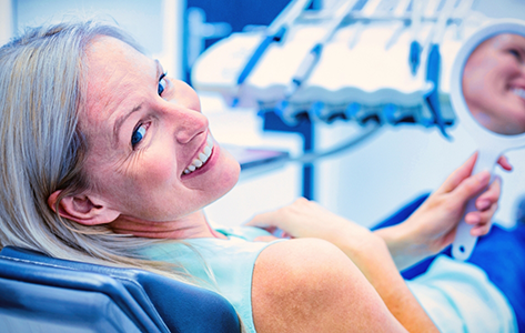 Woman in the dental chair holding a mirror and smiling back over her shoulder