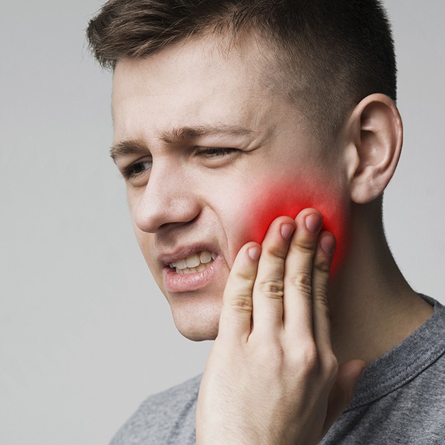 Young man in need of facial trauma treatment holding jaw