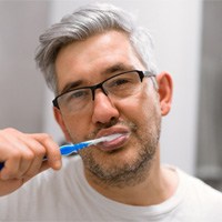 Gray-haired man in white t-shirt brushing his teeth