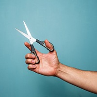 Hand holding scissors against teal background