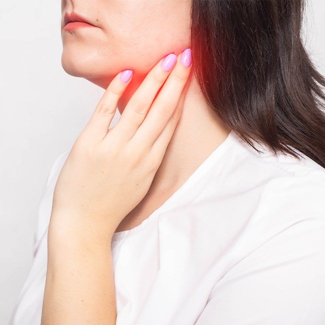 Woman in need of salivary gland cyst and tumor treatment holding her jaw