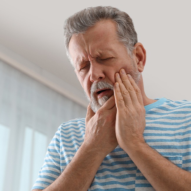 Man in need of skin cyst and tumor treatment holding his cheek