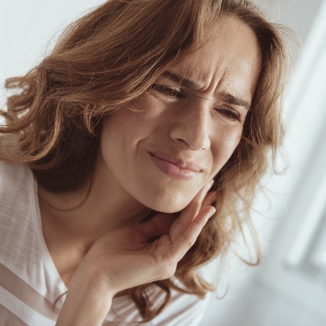 Woman in need of wisdom tooth extraction holding her jaw in pain