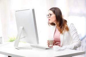 Woman staring at her computer while holding her coffee cup