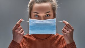 woman in sweater carefully putting on face mask