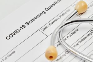 oral surgeon’s COVID-19 screening questionnaire form under stethoscope