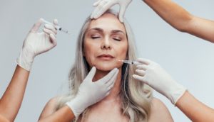 Two pairs of hands inserting BOTOX into middle-aged woman