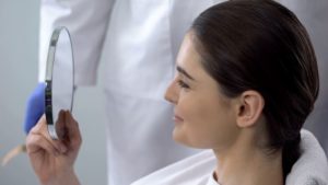 Woman looking in mirror after treatment for facial trauma