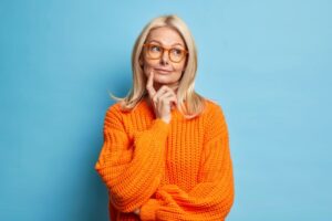 Mature woman in orange sweater with curious expression on her face